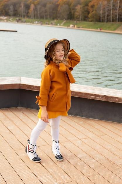 a beautiful blonde girl in a beige coat with a hat on the pier of the city lake nature