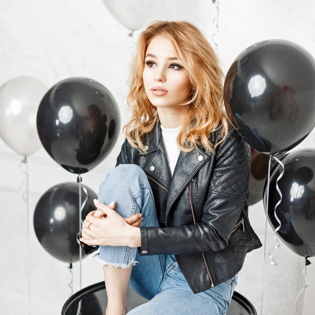 Beautiful blonde girl in a black leather jacket sitting near air balloons