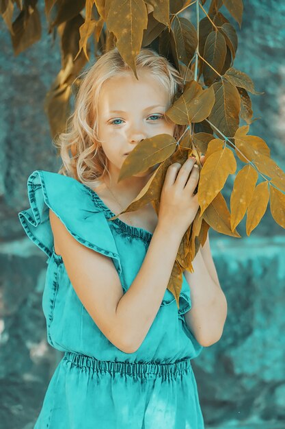 Beautiful blonde girl in a blue dress in the summer in the garden. posing next to foliage. High quality photo