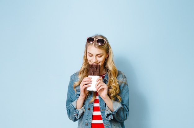 beautiful blonde girl eating chocolate is excited on a blue background