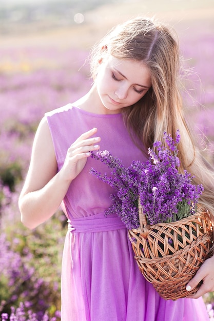 フィールドでラベンダーの花とバスケットを保持している美しいブロンドの女の子