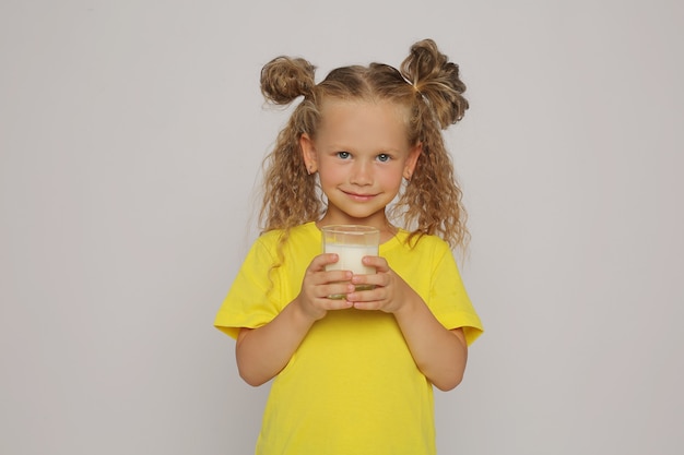 Photo a beautiful blonde girl holds a glass of milk in her hands