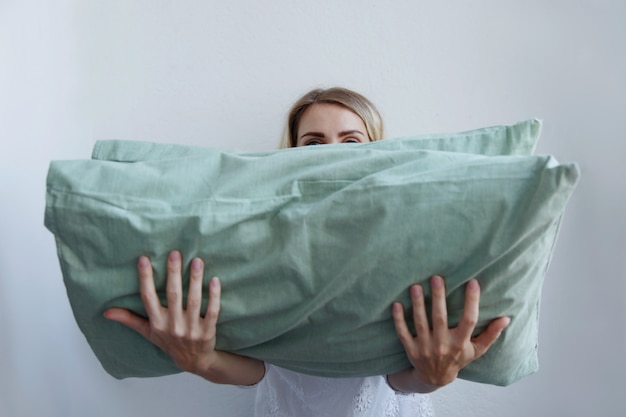 Beautiful blonde girl holds a lot of pillows in her hands. She lies on them with pleasure.
