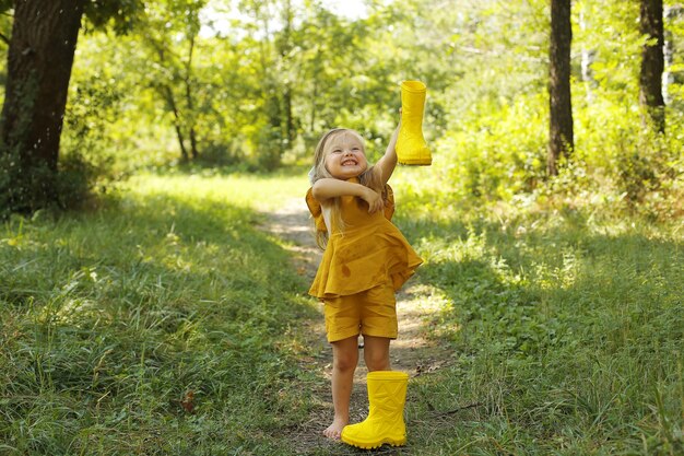 a beautiful blonde girl in a linen suit is standing next to yellow boots in the park