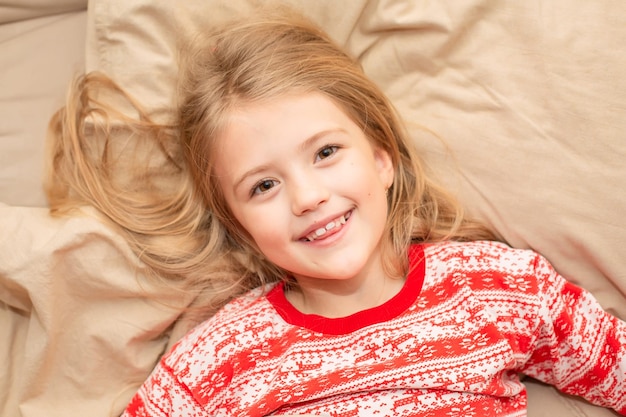 a beautiful blonde girl in New Year's pajamas is lying in a bed with linen bedding