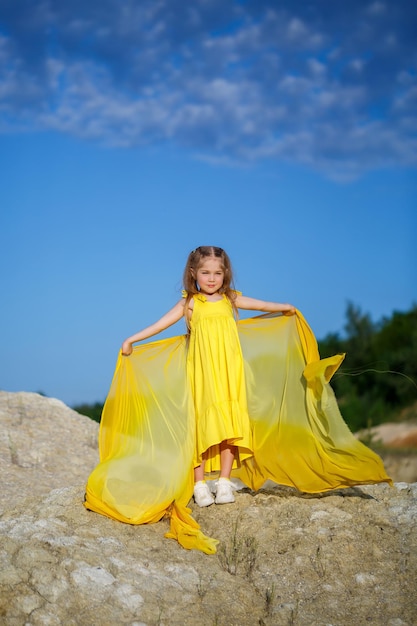 Beautiful blonde girl posing in a yellow dress in nature. Summer photo. Blue sky. Sunny day.