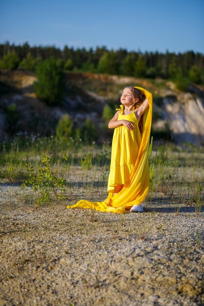 Beautiful blonde girl posing in a yellow dress in nature. Summer photo. Blue sky. Sunny day.