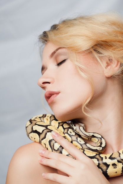 Beautiful blonde girl and python around her body on gray background