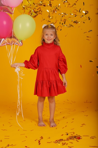 풍선 풍선을 손에 들고 빨간 드레스를 입은 아름다운 금발 소녀는 휴일이다