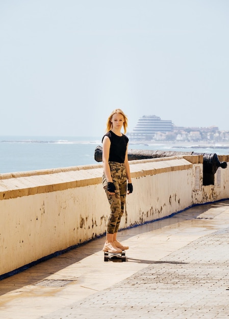 A beautiful blonde girl on skateboard in summer hot day on seafront