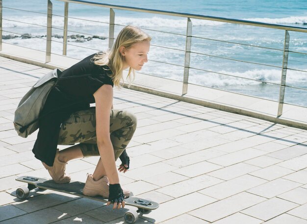 Красивая блондинка на скейтборде в жаркий летний день на берегу моря