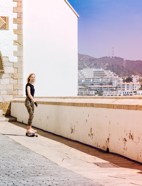 Una bella ragazza bionda su skateboard in una calda giornata estiva sul lungomare