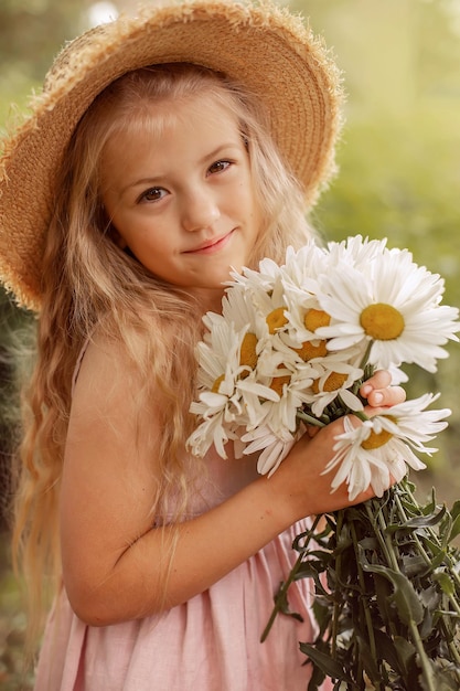 a beautiful blonde girl in a straw hat with white daisies in her hands