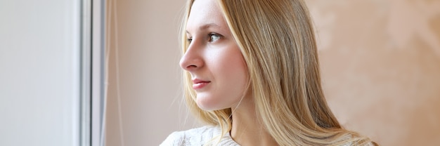 La bella ragazza bionda guarda meditatamente fuori dalla finestra