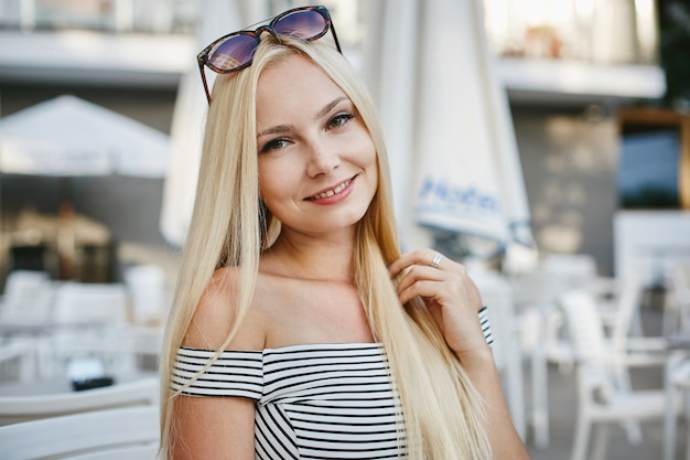 Beautiful blonde girl in the trendy striped short dress and in fashionable sunglasses