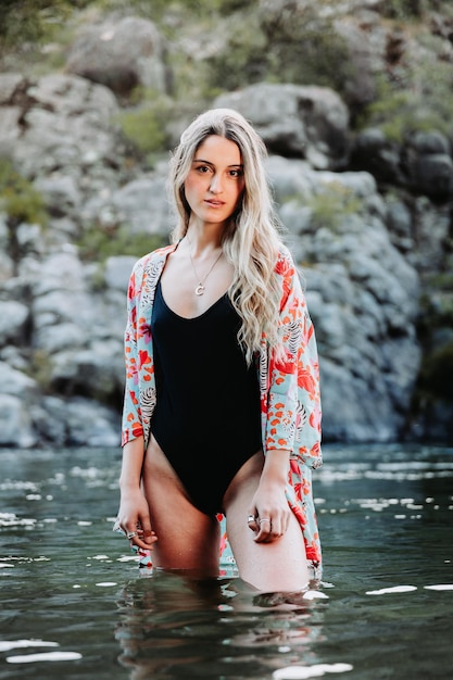 Bella ragazza bionda, che usa un bikini e un kimono floreale, con le gambe nell'acqua.