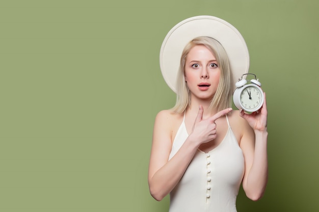 Beautiful blonde girl in white hat and dress with alarm clock