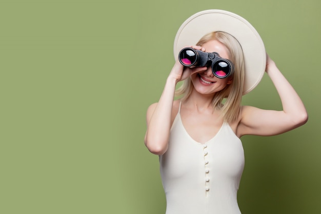 Beautiful blonde girl in a white hat and dress with binoculars