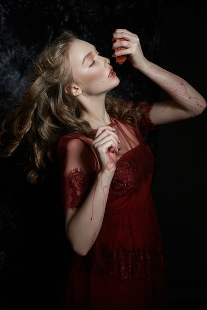 Beautiful blonde girl with pomegranate fruit in her hands. Spring portrait of a girl in a red dress breaking a pomegranate, juice flowing down her hands