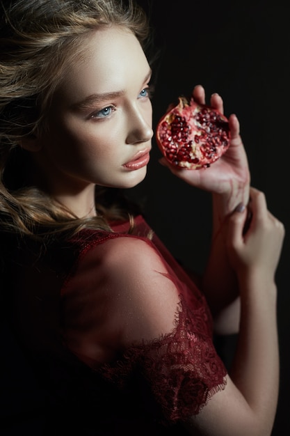 Foto bella ragazza bionda con frutta melograno nelle sue mani.