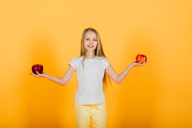 Beautiful blonde girl with red apple in studio, yellow background