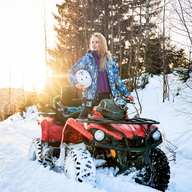 Beautiful blonde girl with red ATV in winter in the mountains