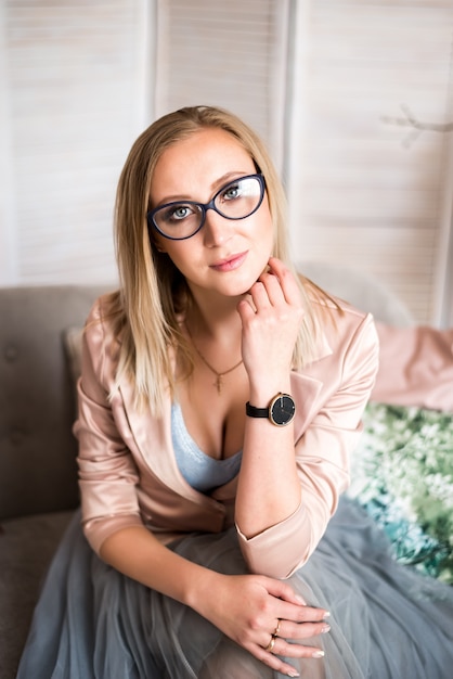 Beautiful blonde in glasses with a pen in her hands on a light background. Businesswoman.