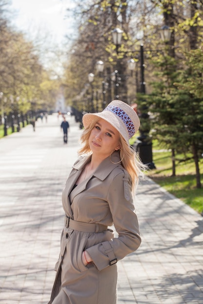 Красивая блондинка в плаще и шляпе на прогулке в парке