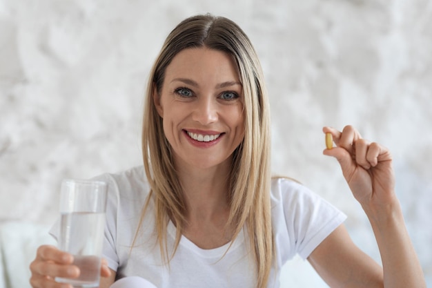 錠剤と水のガラスを保持している美しいブロンドの女性