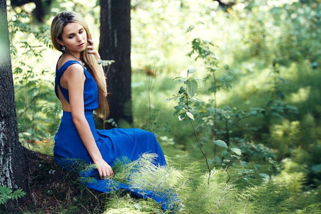 Beautiful blonde in a long blue dress in forest