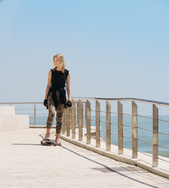 Foto bella bionda su uno skateboard in una calda giornata estiva in riva al mare