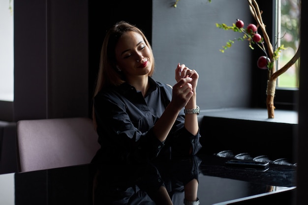 Beautiful blonde smiling girl wearing trendy black shirt sitting in cafe and listening music.