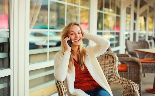 beautiful blonde smiling young woman calling on mobile phone sitting on chair waiting in city cafe