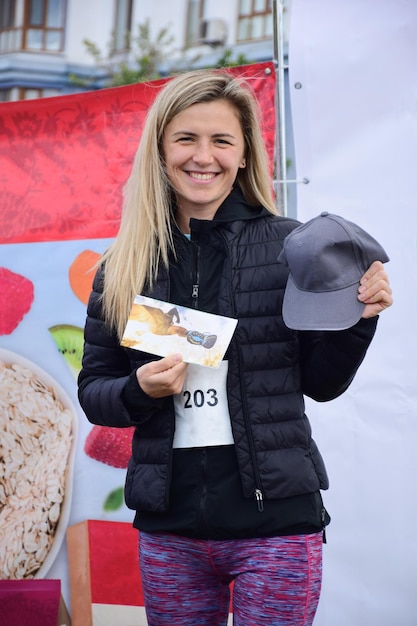 A beautiful blonde sportswoman from Nordic walking on a pedestal shows the won prize and smiles