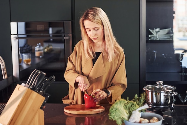 Фото Красивая блондинка стоит в помещении на кухне и готовит еду