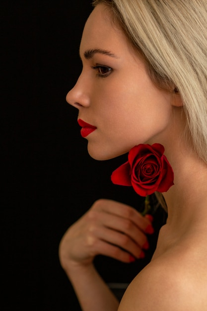 Красивая блондинка стильно позирует с красной розой на темном