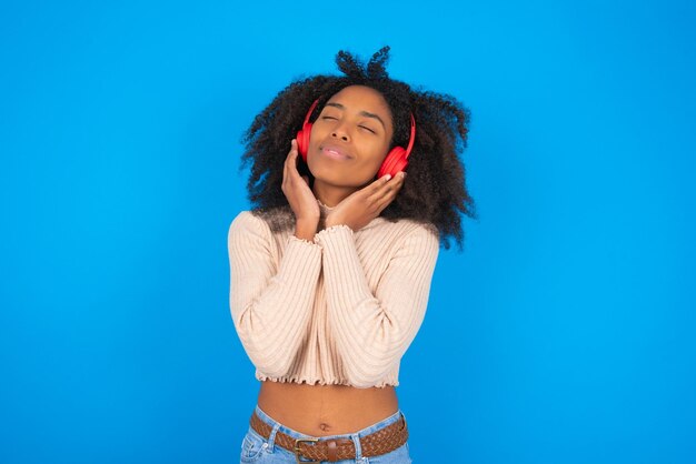 beautiful blonde teen girl listening to music wearing red wireless headphones pointing aside