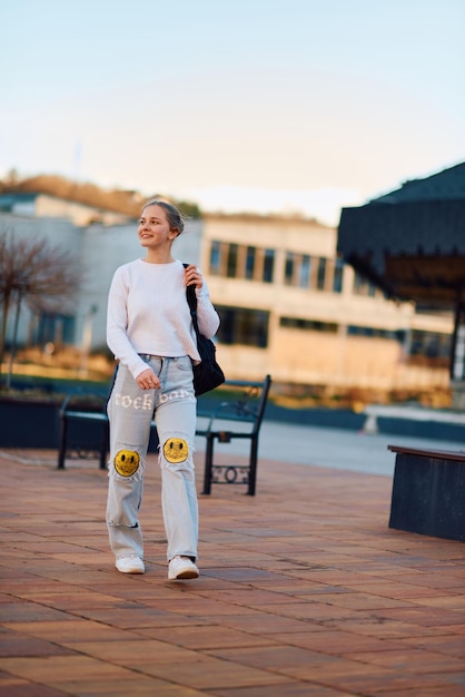 A beautiful blonde teenager returns home from school during the sunset carrying her school backpack