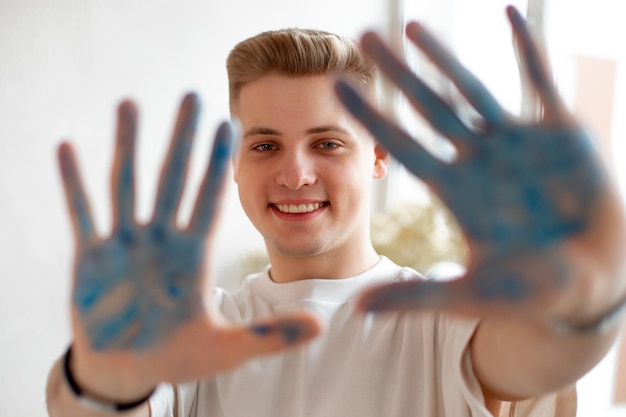 Beautiful blonde toothy smile young man drawing male looking at camera and show defocused blue paint