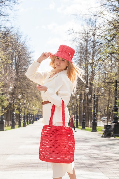 Bella bionda in una passeggiata con una borsa e un cappello rosso fatto a mano