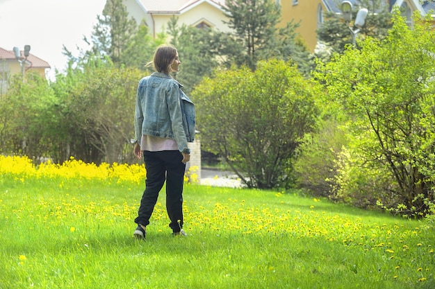 美しいブロンドは黄色い花と明るい緑の芝生の上を歩きます