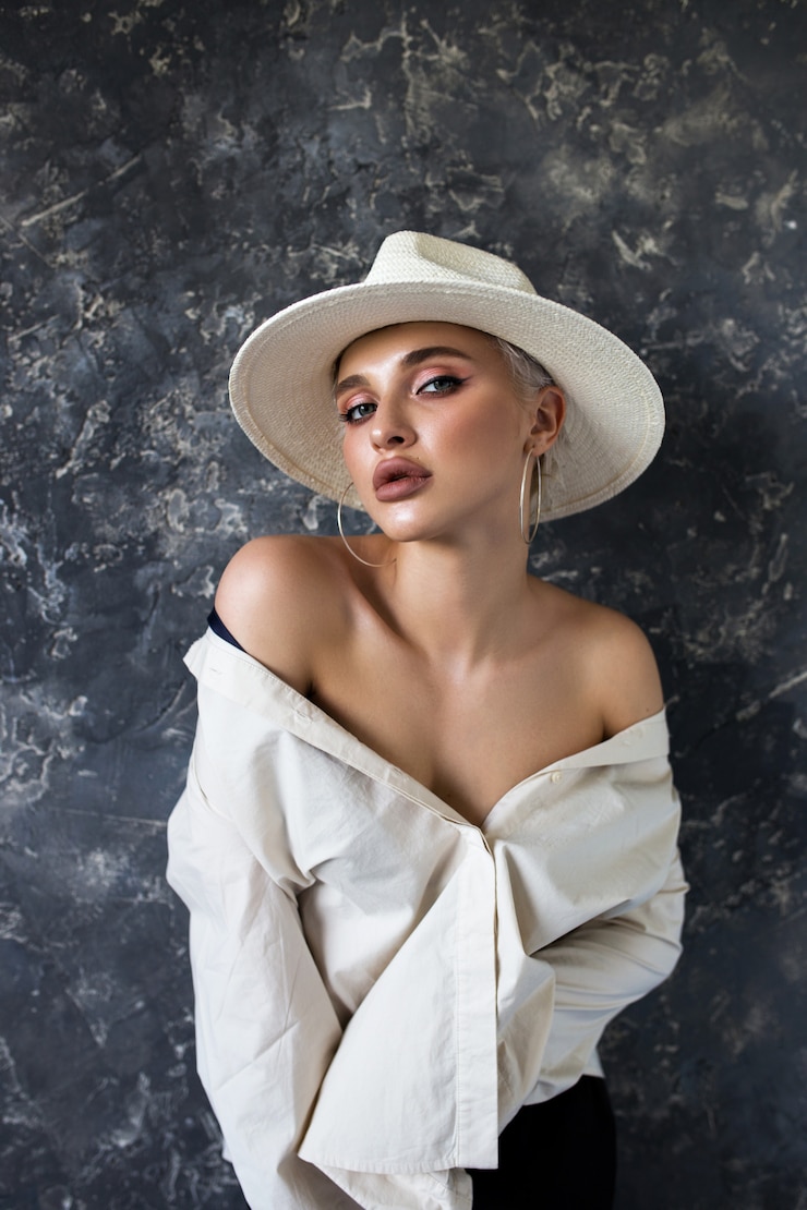 Photo beautiful blonde in a white shirt with black pants and a white hat on a blue. 