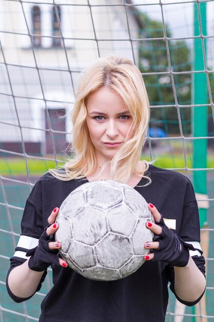 Photo beautiful blonde with a ball at the football goal