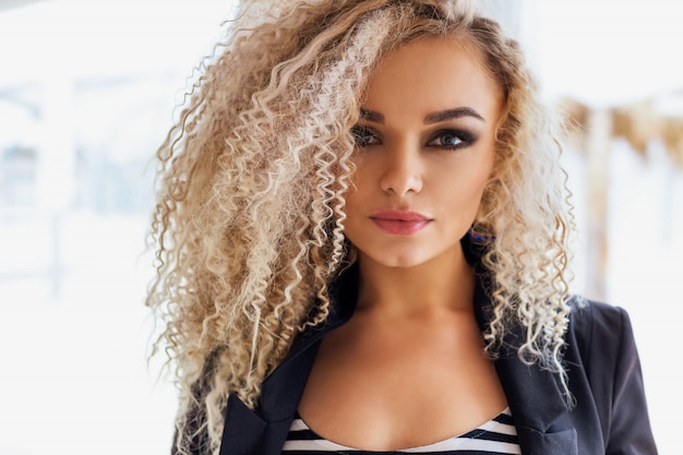  beautiful blonde with bright makeup and curly hair posing in a black jacket 