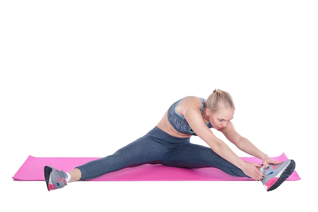 Beautiful blonde woman does exercises on fitness mat on white background stretching