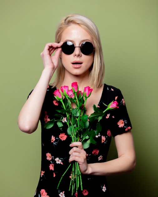 Beautiful blonde woman in dress with roses on green wall