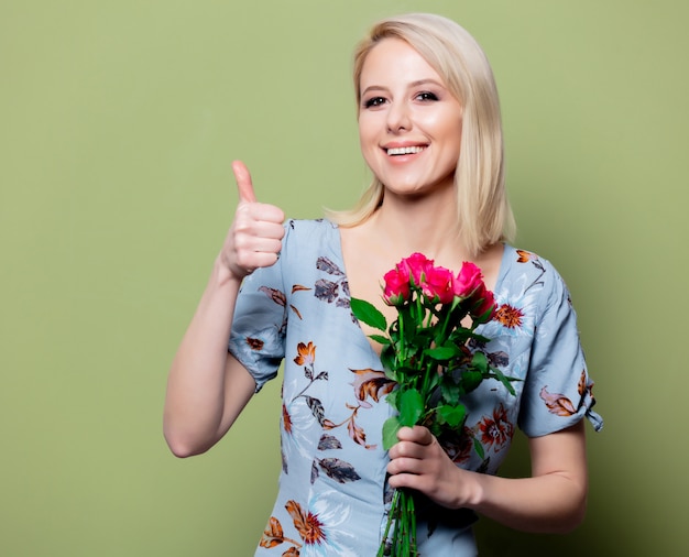 Beautiful blonde woman in dress with roses on green wall