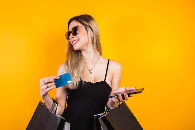 Beautiful blonde woman dressed in black carrying black shopping bags with credit card