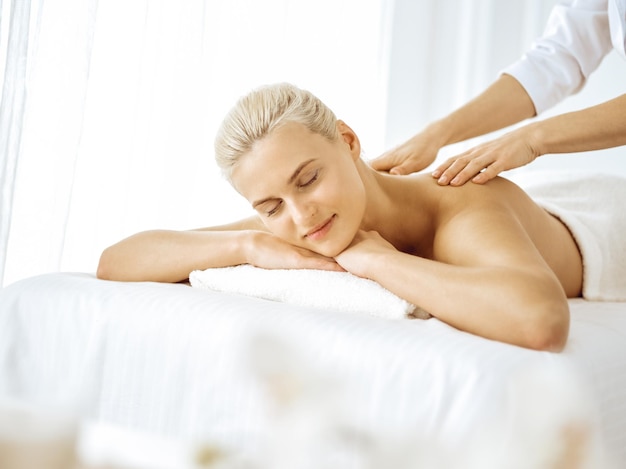 Beautiful blonde woman enjoying back massage with closed eyes. Spa salon concept.