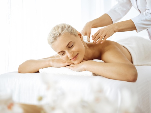 Beautiful blonde woman enjoying back massage with closed eyes. Spa salon concept.